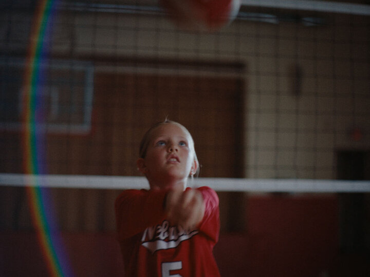 Girl bumping volleyball in high school gym with lens flare